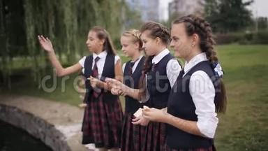 穿校服的学生在学校院子里的池塘里喂鸭子。 女子学院的女学生穿着同一所学校